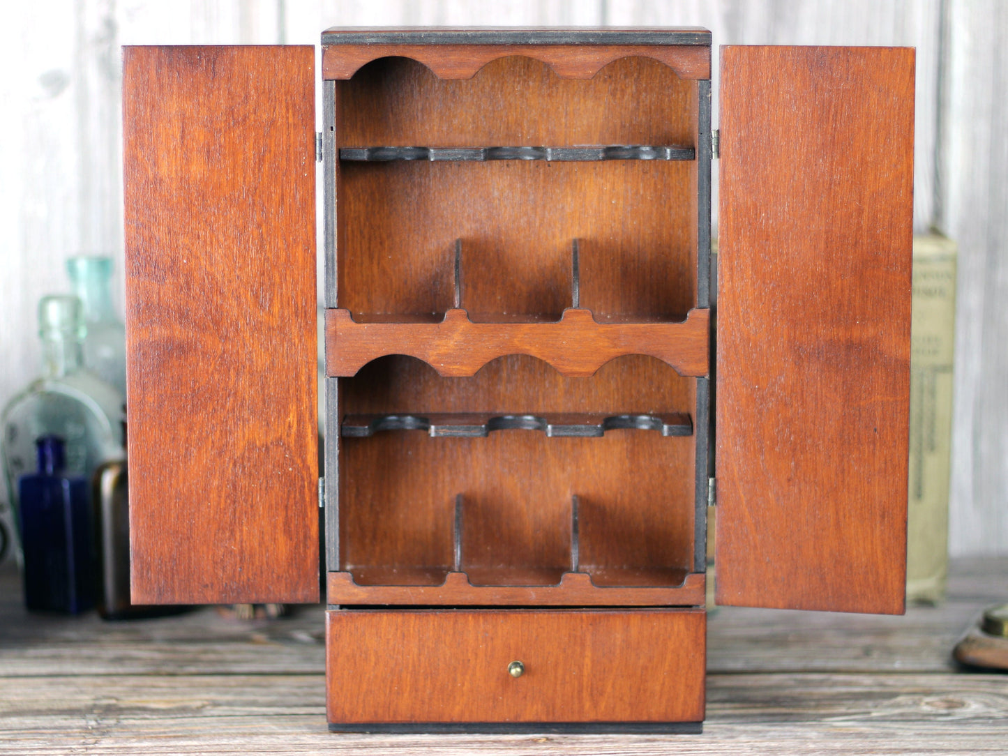 Wooden apothecary cabinet with drawer and holding six brown medicine bottles with glass stoppers