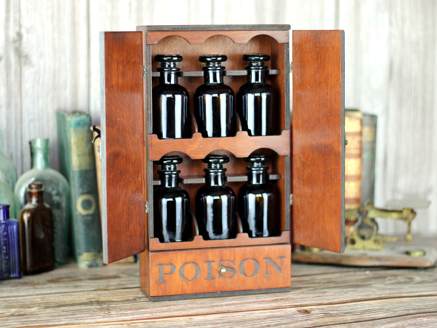 Wooden apothecary cabinet with skull engraving and poison drawer holds six brown medicine bottles with glass stoppers