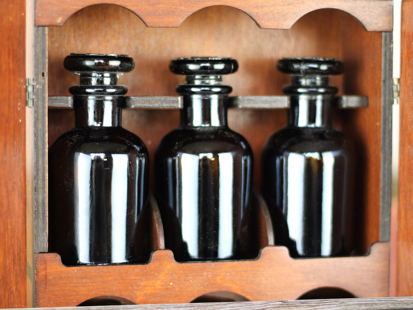 Wooden apothecary cabinet with skull engraving and poison drawer holds six brown medicine bottles with glass stoppers