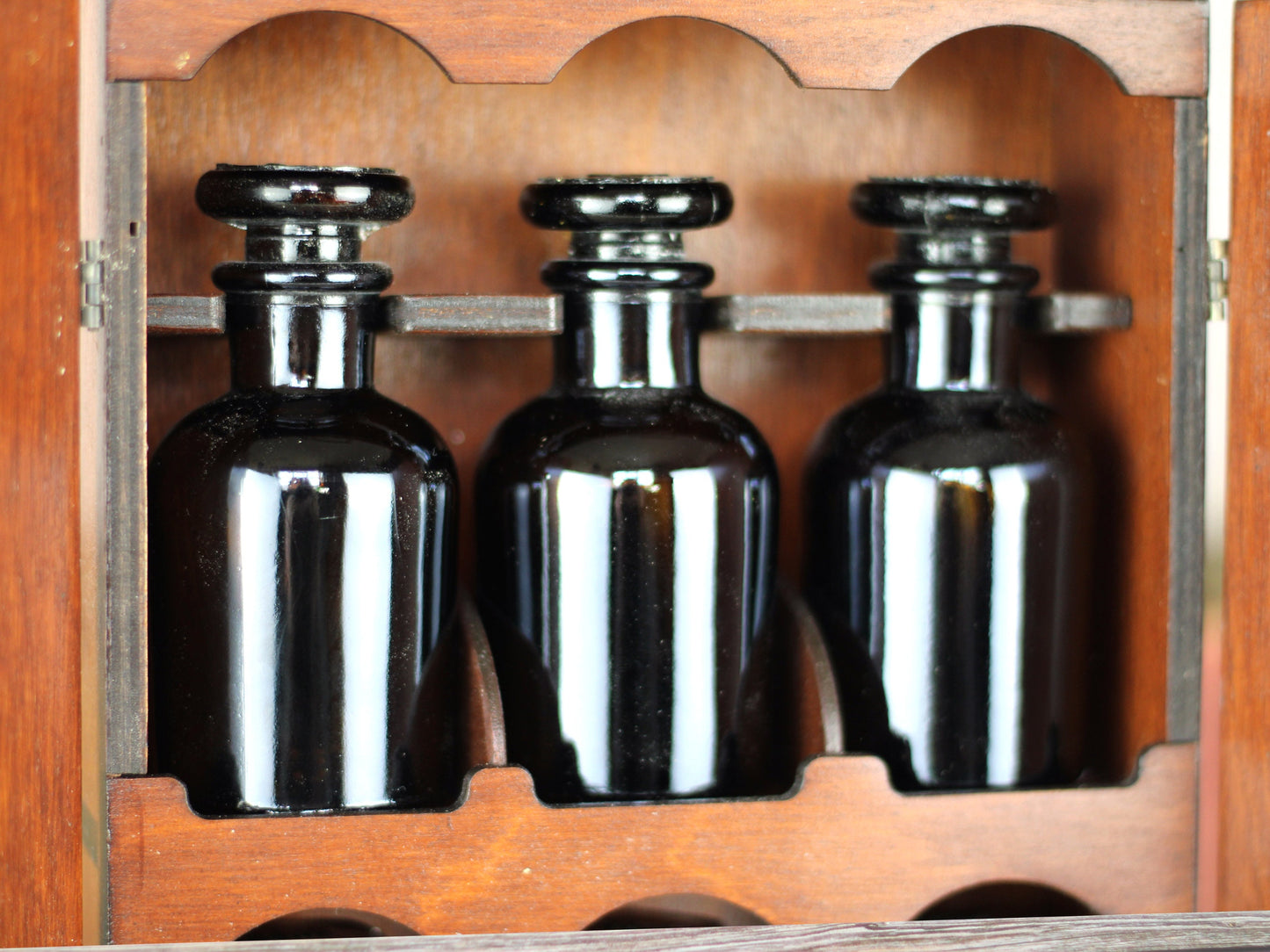 Wooden apothecary cabinet with slatted doors, drawer and 6 brown medicine bottles with glass stoppers