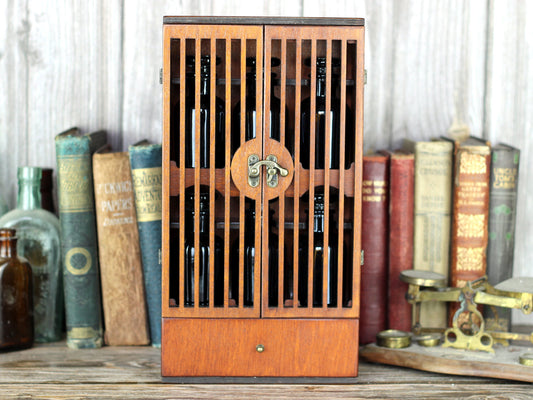 Wooden apothecary cabinet with slatted doors, drawer and 6 brown medicine bottles with glass stoppers